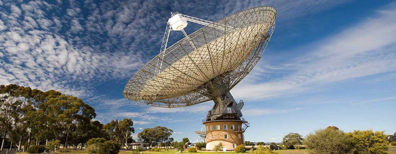 Parkes Radio Telescope surrounded by grass and trees - the Dish shop - blue sky background and scattered white clouds